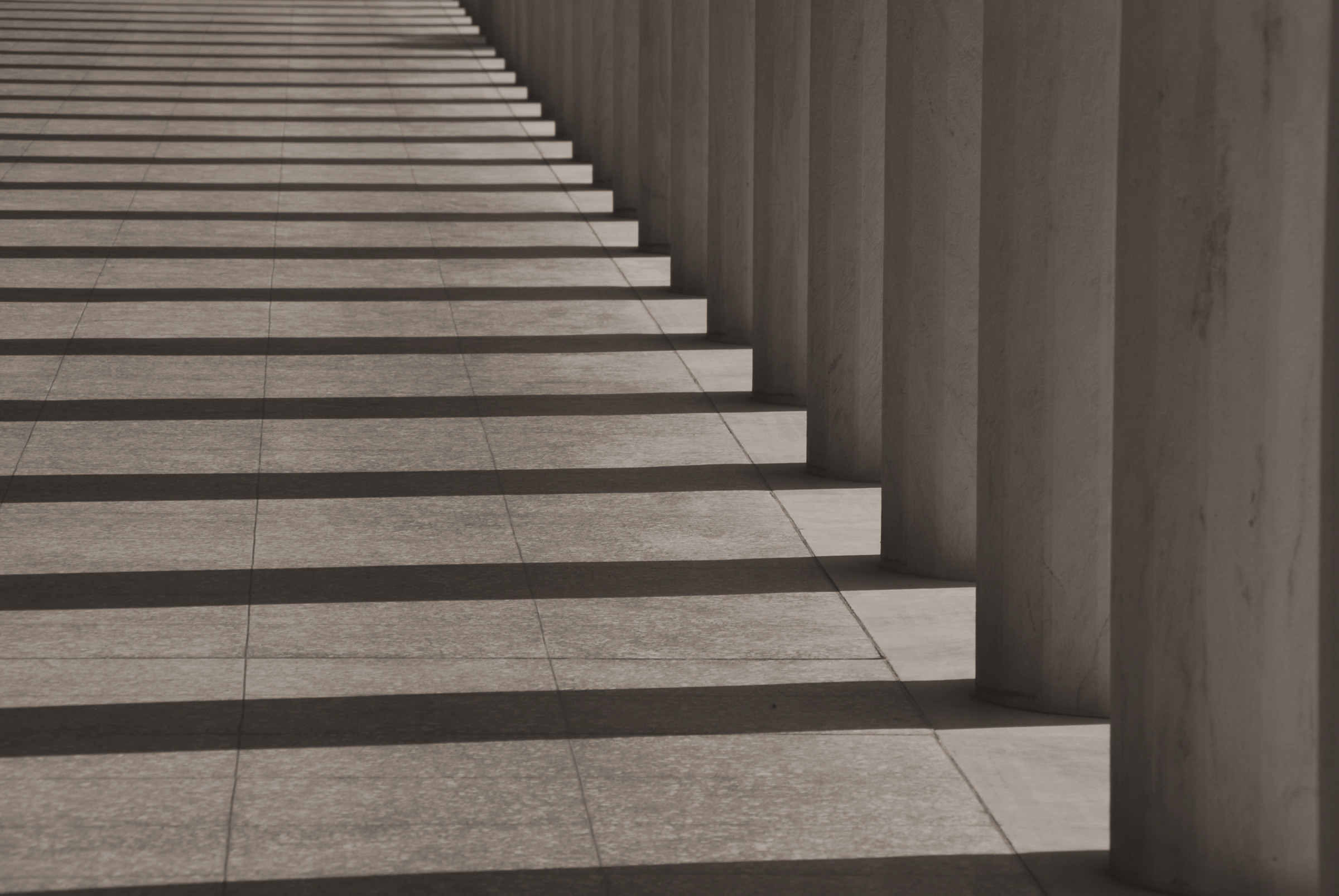 Shadows of a long row of columns falling across stone paving